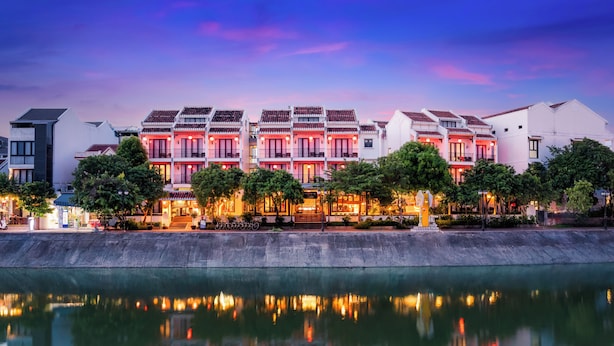 Un hotel frente al agua con arquitectura tradicional, su reflejo en el agua y vistas al cielo.
