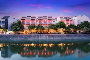 Um hotel à beira-mar com arquitetura tradicional, um reflexo na água e vista para o céu.