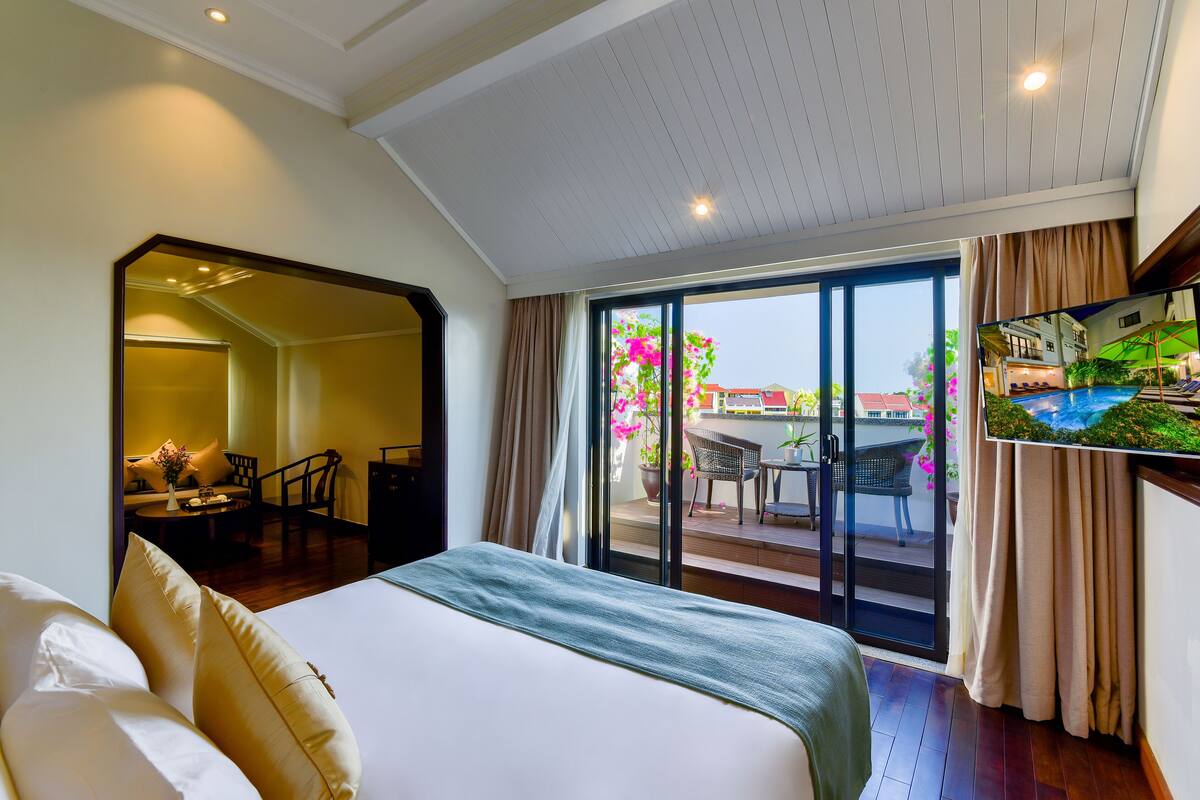 Habitación de hotel con una cama grande, un televisor en la pared y una puerta corrediza de vidrio que da a un área exterior con piscina y sillas.