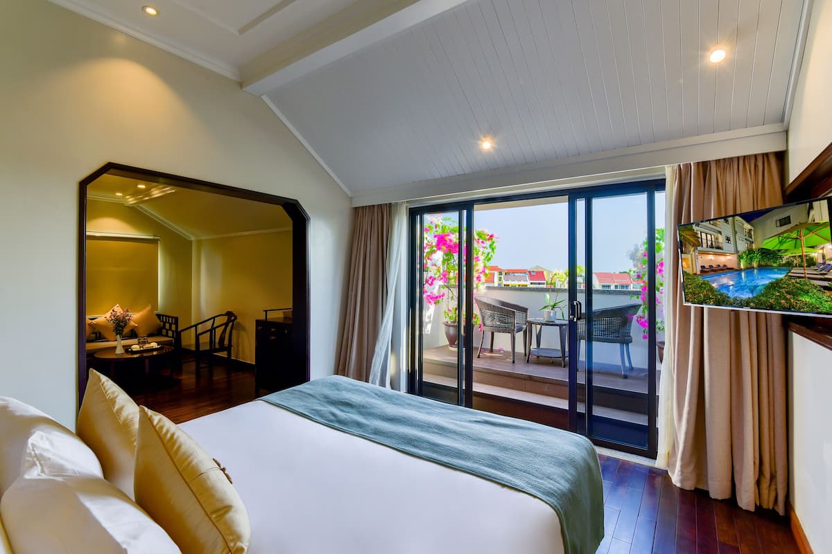 Habitación de hotel con una cama grande, un televisor en la pared y una puerta corrediza de vidrio que da a un área exterior con piscina y sillas.