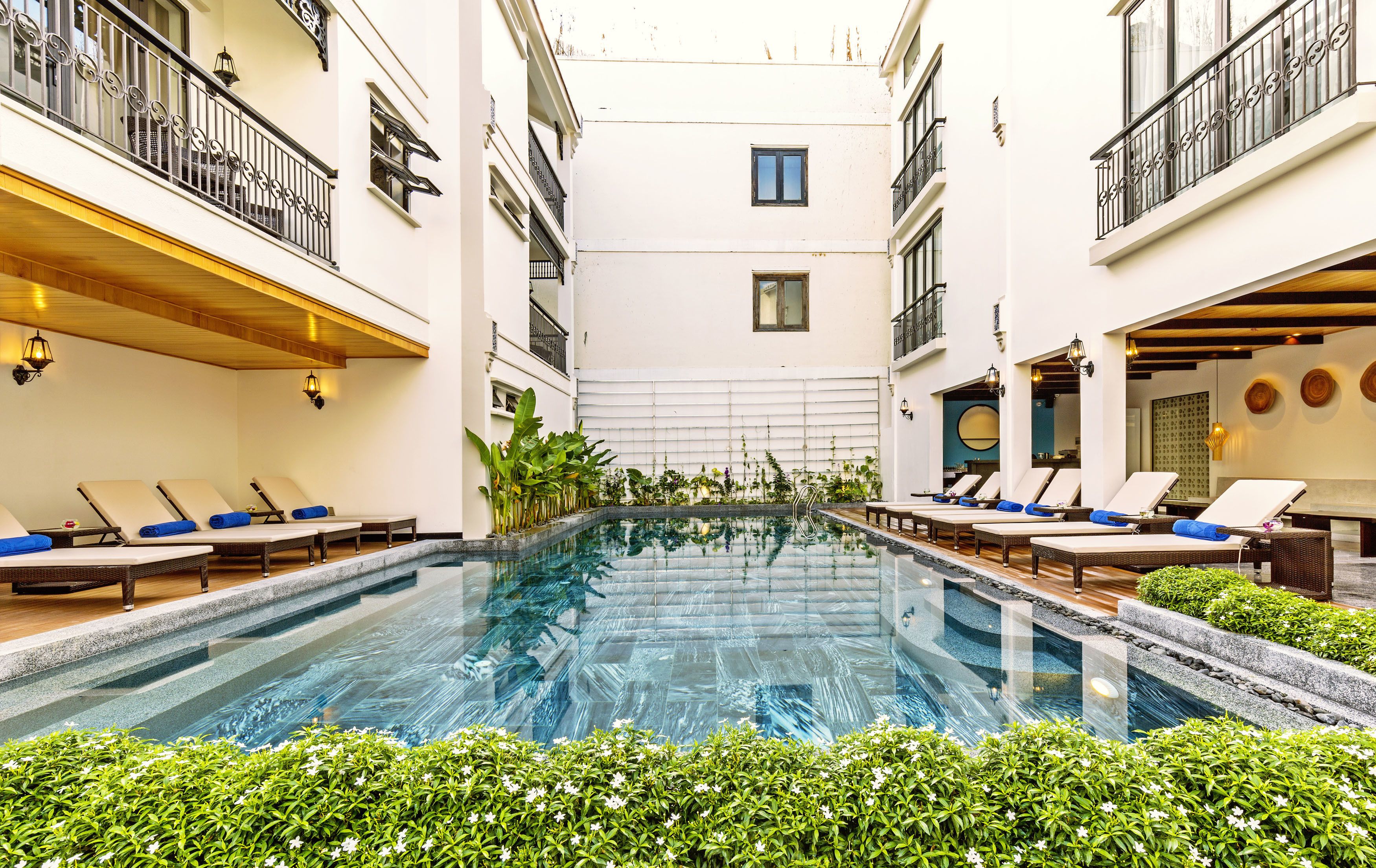 A pool area with lounge chairs and a clear pool, surrounded by greenery and white walls.