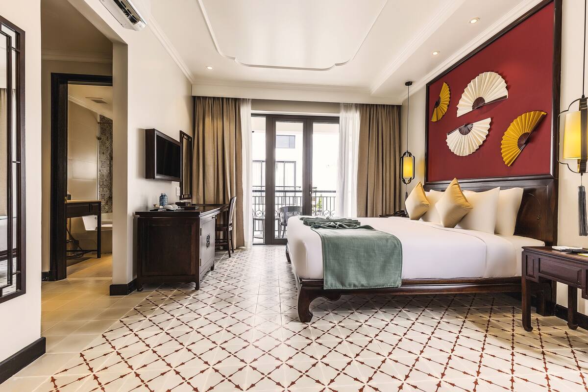 Habitación de hotel con una cama grande, un escritorio, un televisor y un balcón con vistas.