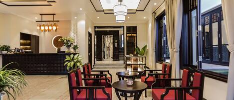 A hotel lobby with red upholstered chairs, a reception desk, and a large window with curtains.