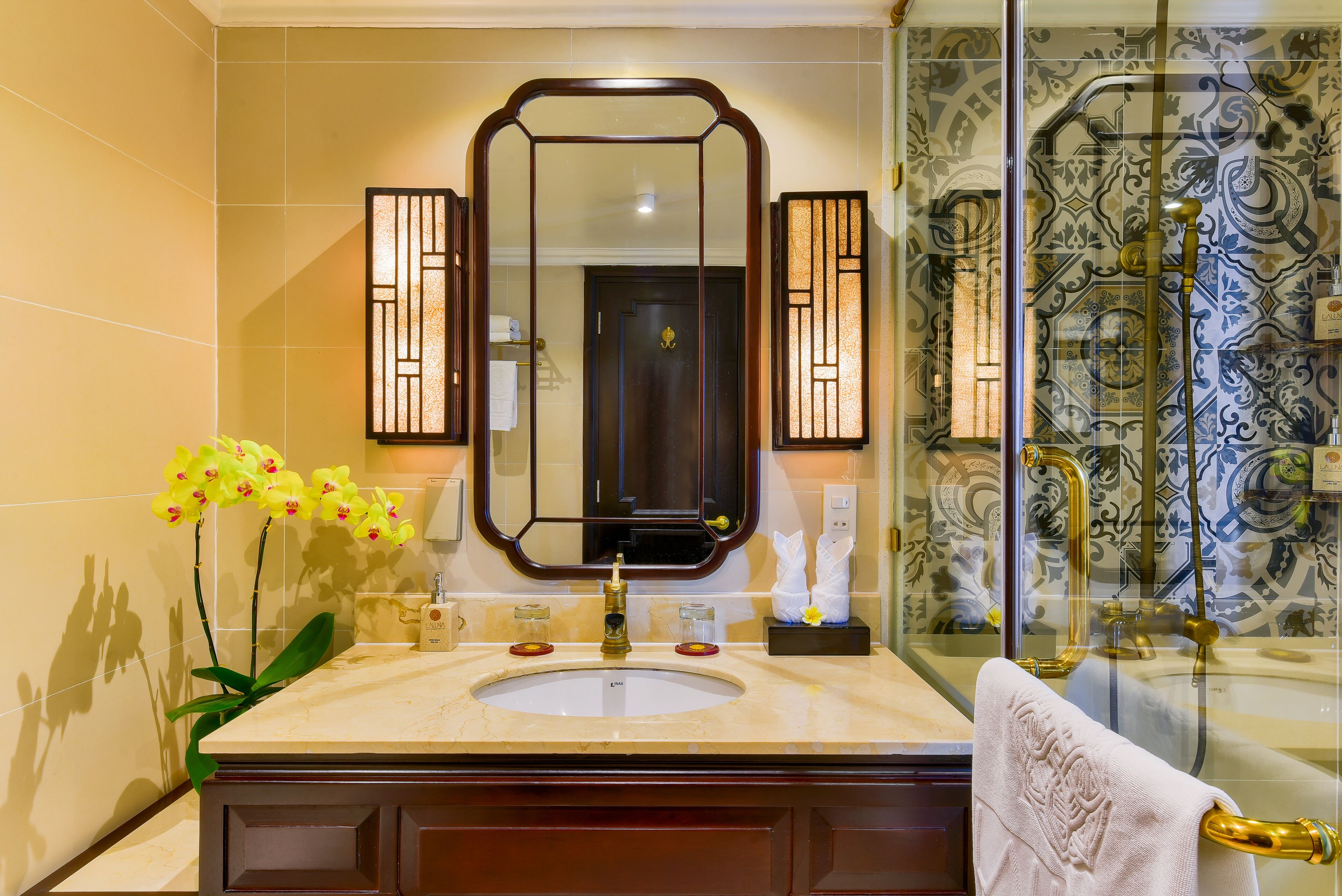A bathroom with a large mirror, a sink, a glass shower enclosure, and decorative tiles.