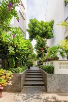 Uma viela estreita com degraus que levam a um edifício, rodeada por vegetação exuberante e plantas em vasos.