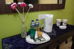 Un meuble-lavabo avec un distributeur d’eau, deux bouteilles d’eau, un verre, un sachet de café et une tasse.