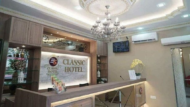 A reception area with a chandelier, a reception desk, and a wall-mounted TV. - Ghazrin's Classic Hotel (Johor Bahru)