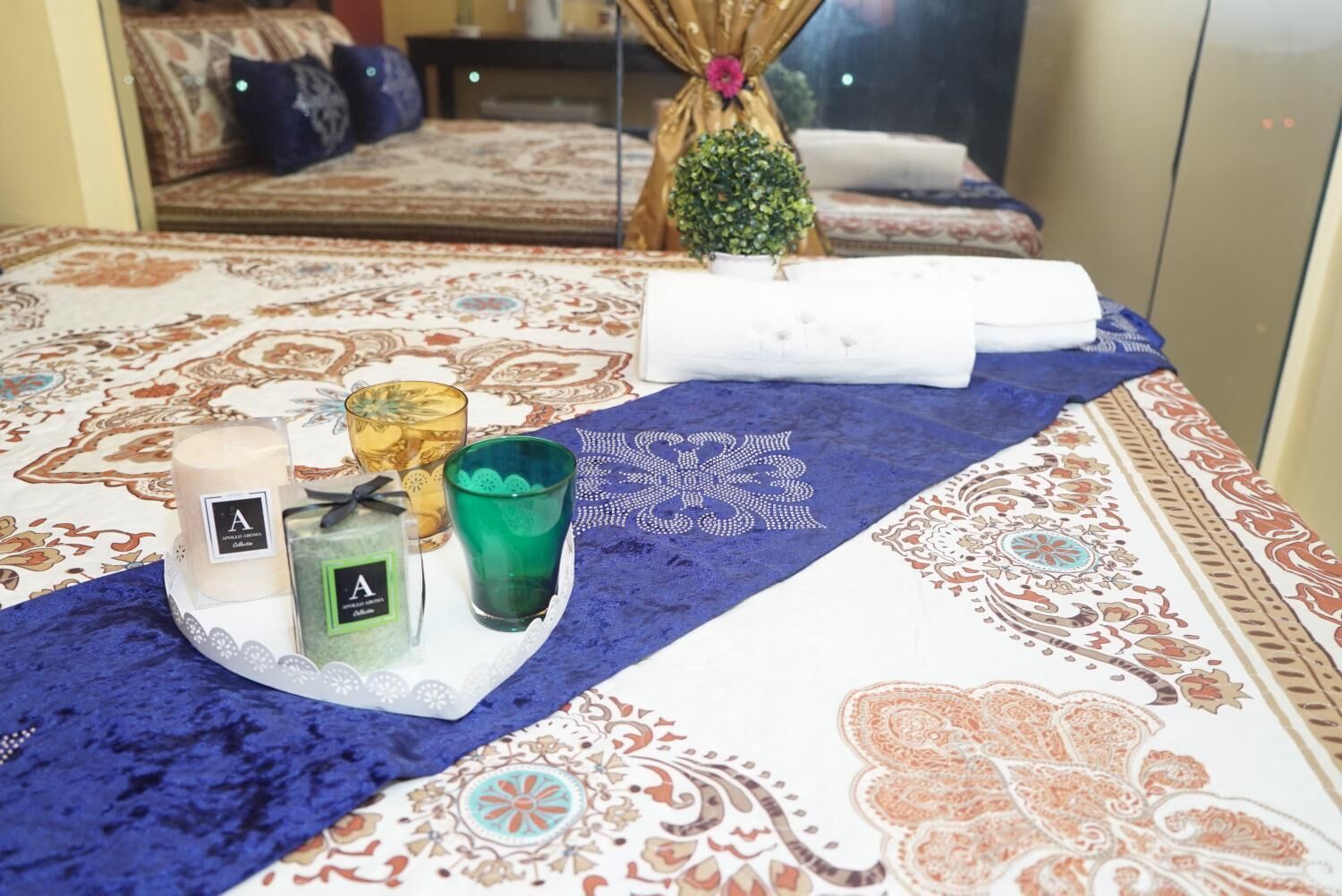 A neatly made bed with a patterned bedspread, a decorative pillow, and a small potted plant on the side.