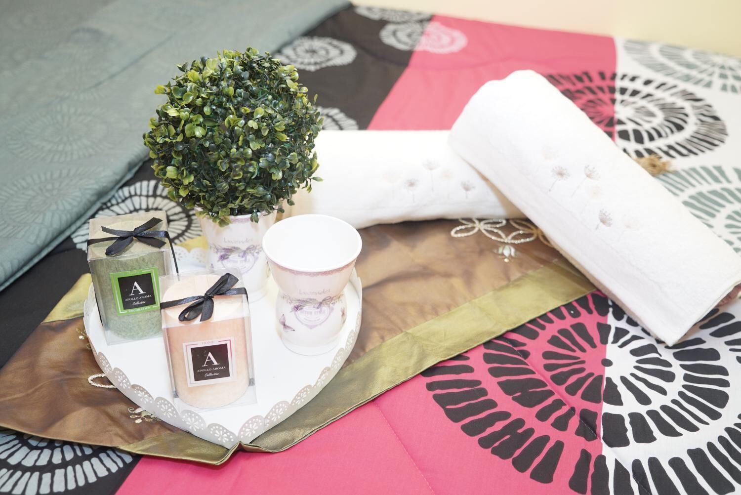 A tray with scented candles, a small potted plant, and a decorative item on a patterned fabric.