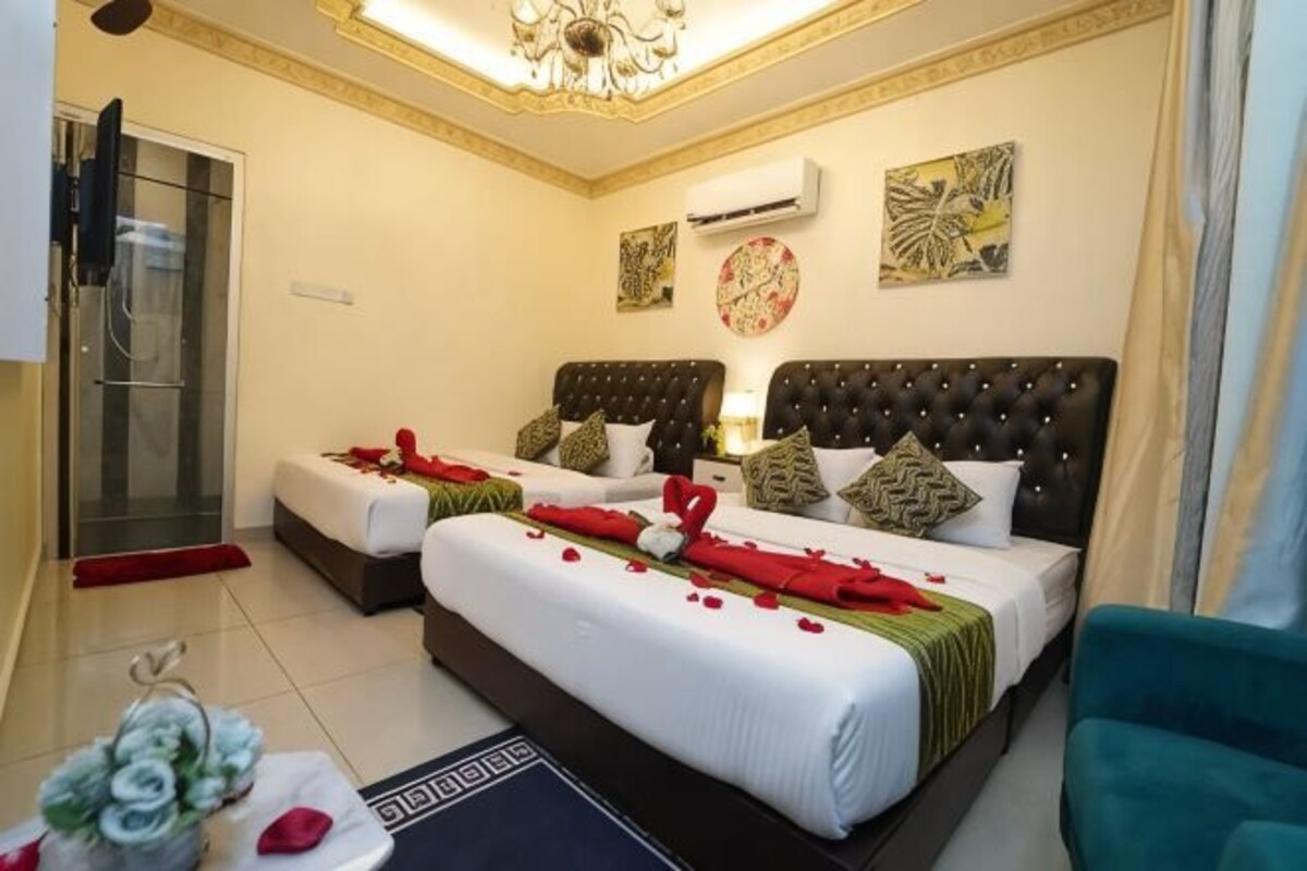 A hotel room with two beds, a sitting area, a TV, and a shower area.