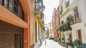 A cobblestone street lined with colorful buildings, featuring balconies with plants and a clear sky. - OFFER, ELEGANCE AND COMFORT, A DREAM IN THE CENTER OF SEVILLE (Sevilla)