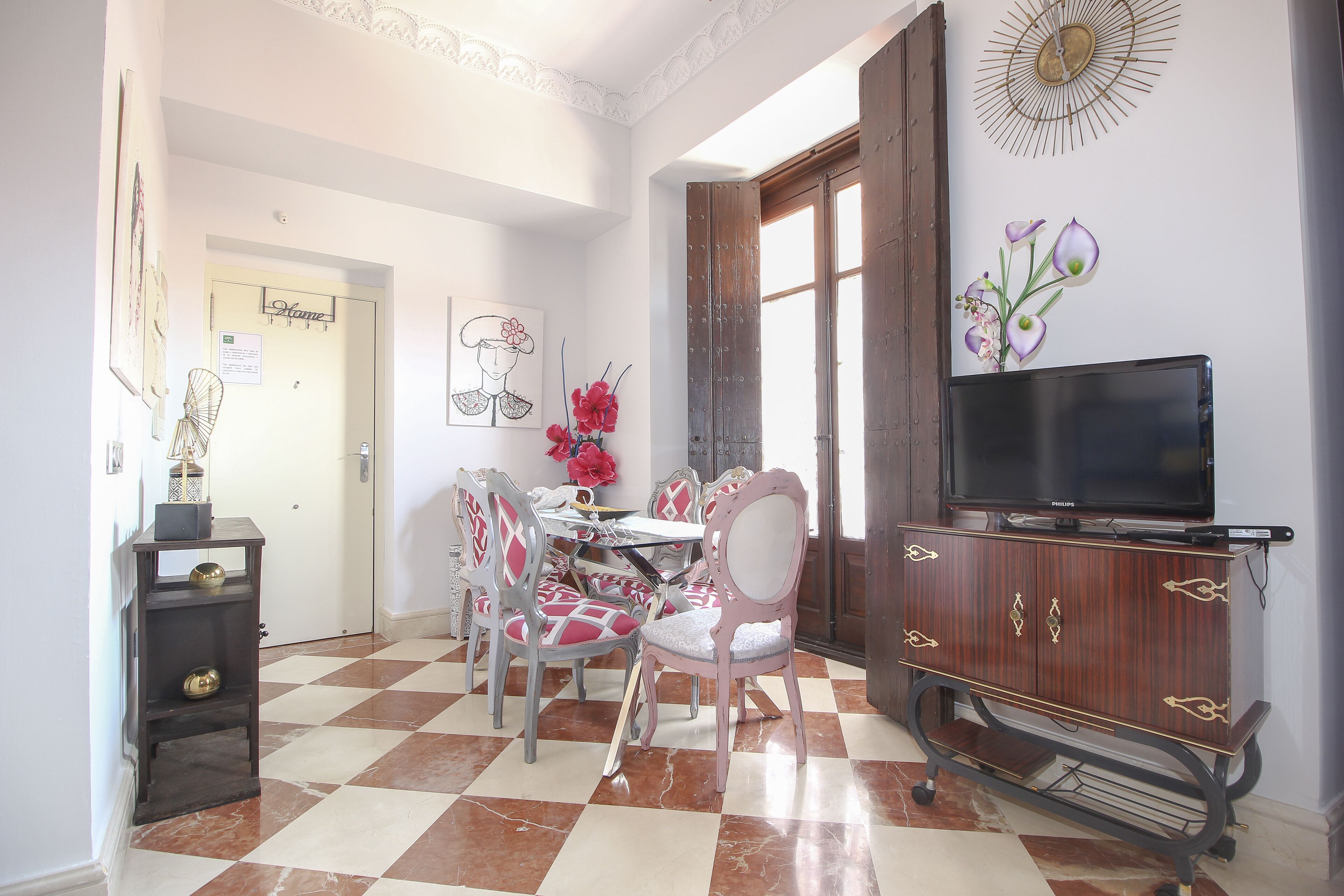 Un comedor con piso a cuadros, un televisor sobre un mueble de madera y una puerta con un letrero que dice 'Home'.