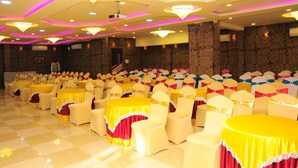 A banquet hall with rows of tables and chairs, chandeliers, and a checkered floor.