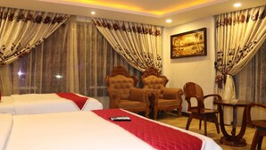 A hotel room with two beds, a dining table, and two ornate chairs.
