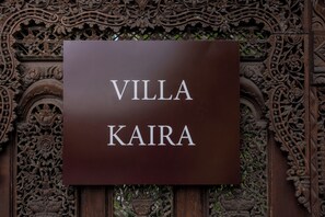 Kyltti, jossa lukee ”VILLA KAIRA”, on sijoitettu koristeellisen puisen taustan eteen.