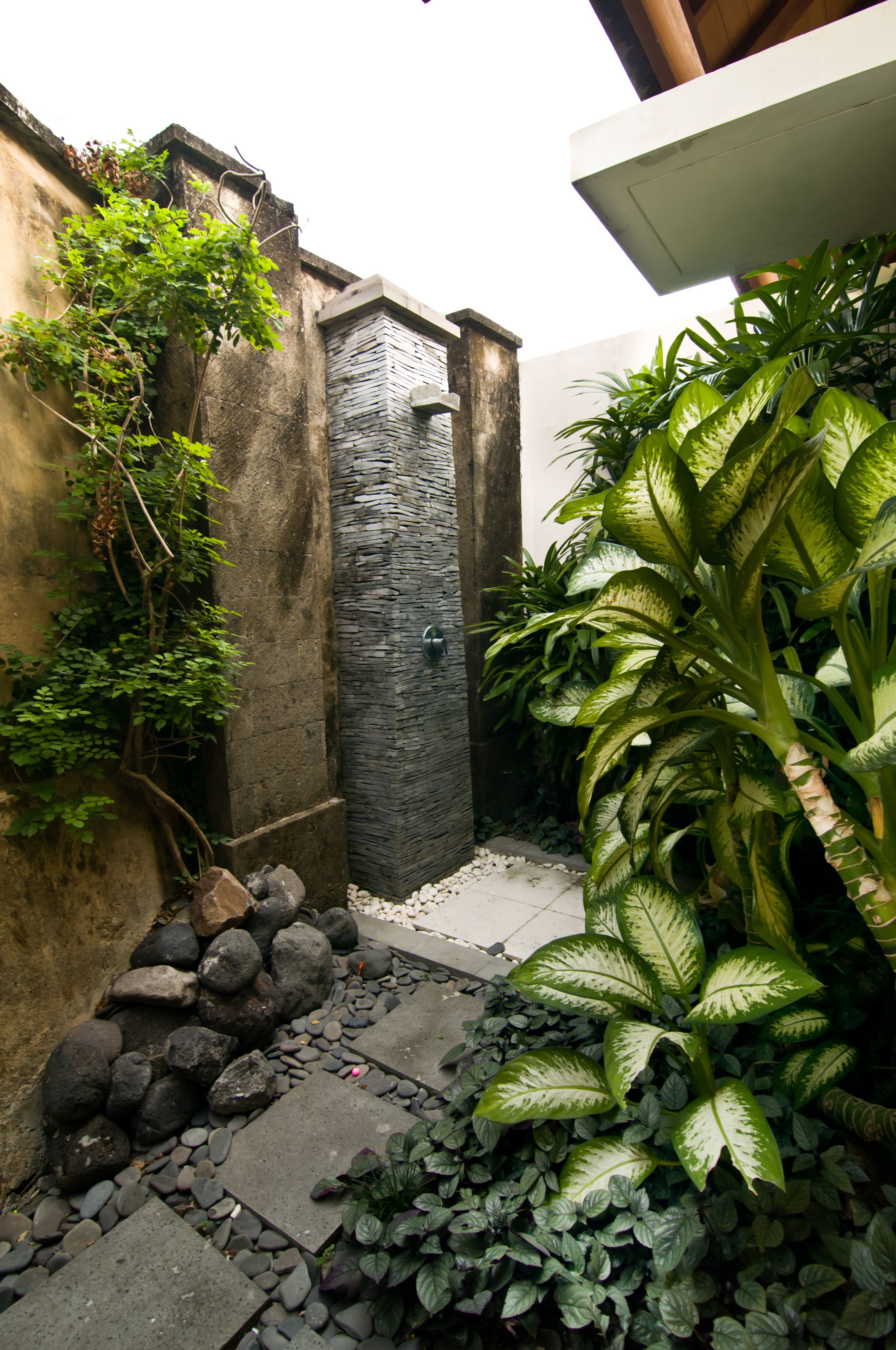 Un étroit sentier extérieur bordé d’un mur de pierre et agrémenté d’un petit jardin planté de différentes espèces.