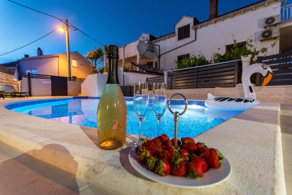 Escena junto a la piscina con una botella, vasos y un plato de fresas.