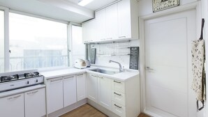 A modern kitchen with white cabinets, a gas stove, a sink, and a window. - Tribear House 1 (Seoul)
