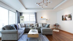 A modern living room with a sectional sofa, a coffee table, and a decorative ceiling light. - Tribear House 1 (Seoul)