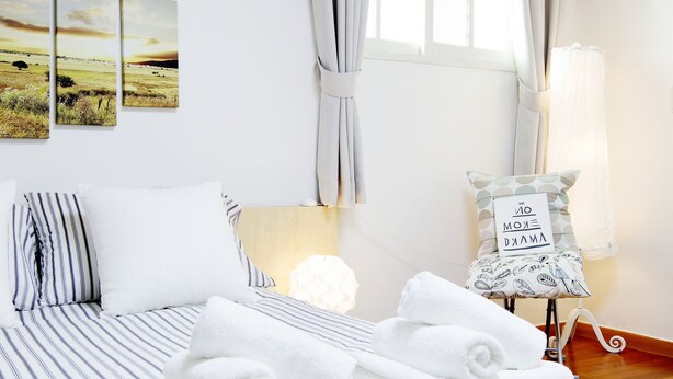 A hotel room with a bed, pillows, a bedside table with a lamp, a wall-mounted air conditioner, and a window with curtains. - Tribear House 1 (Seoul)
