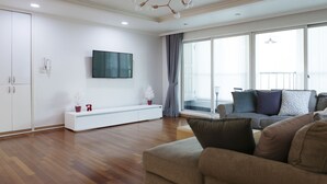 A modern living room with a sofa, a TV mounted on the wall, and a sliding glass door leading to a balcony. - Tribear House 1 (Seoul)
