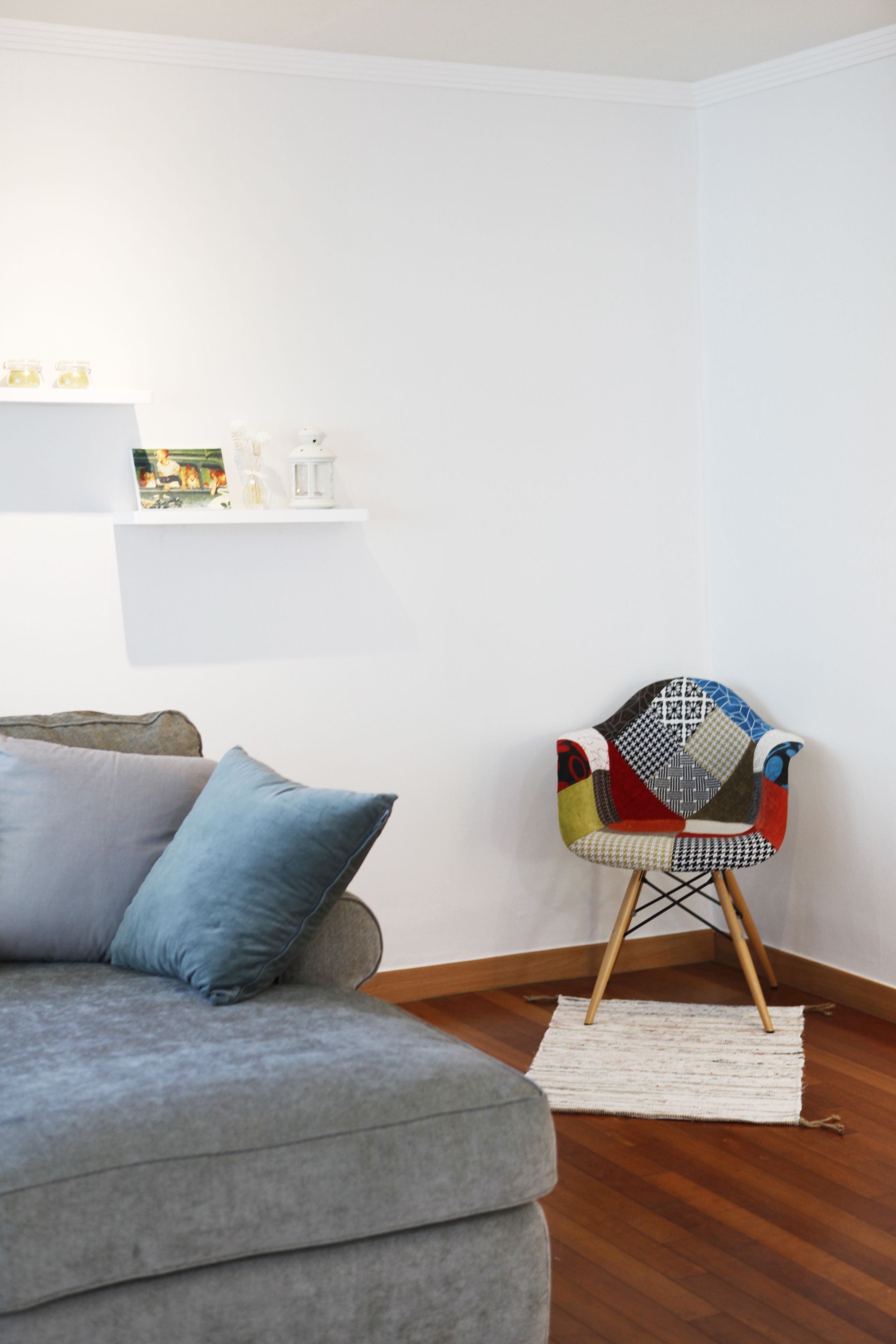 Un soggiorno moderno con un divano grigio, una poltrona colorata e uno scaffale bianco con oggetti decorativi.