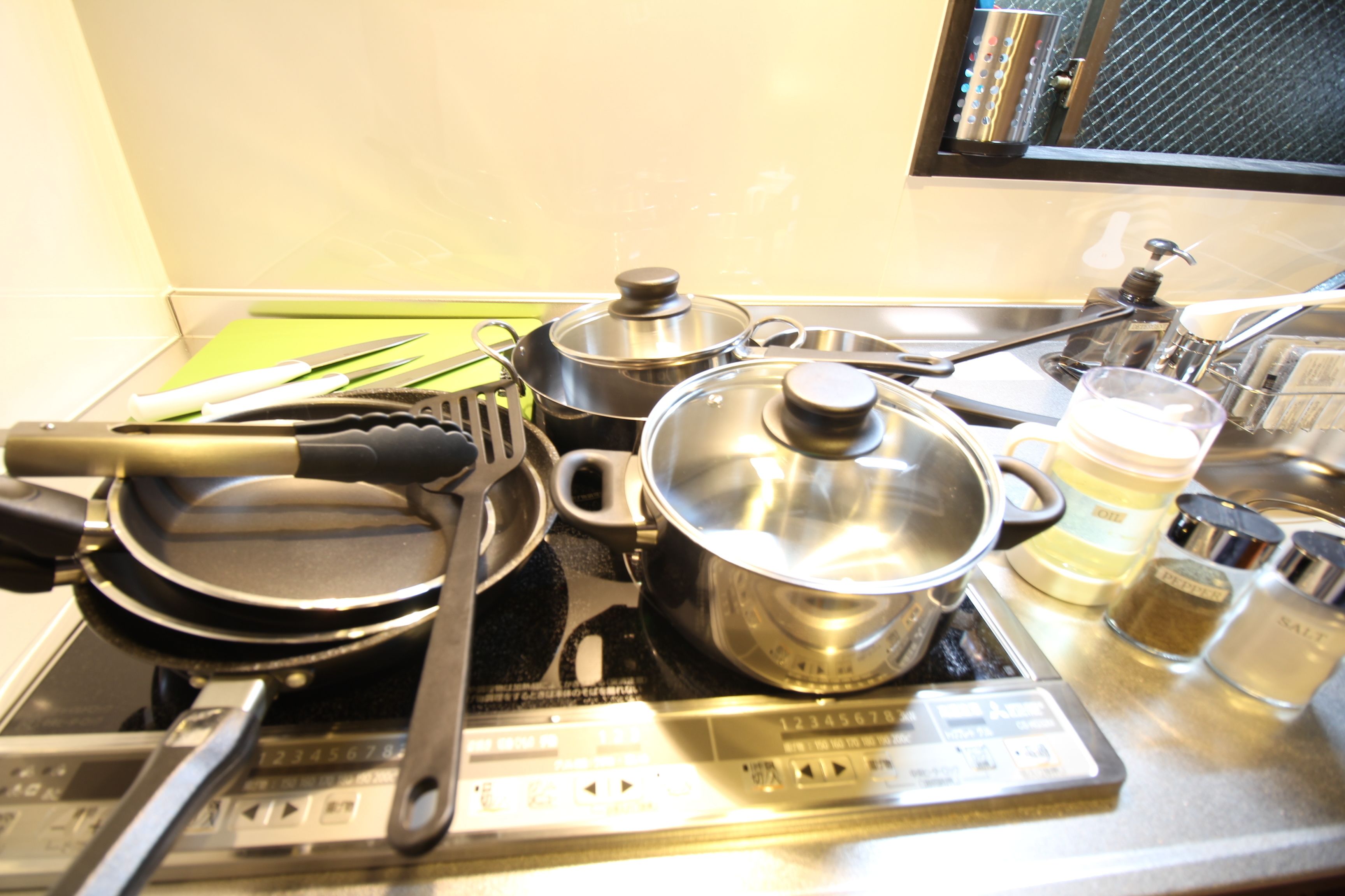 A kitchen counter with a stove, pots, pans, a frying pan, a spatula, a glass of water, and a salt container.