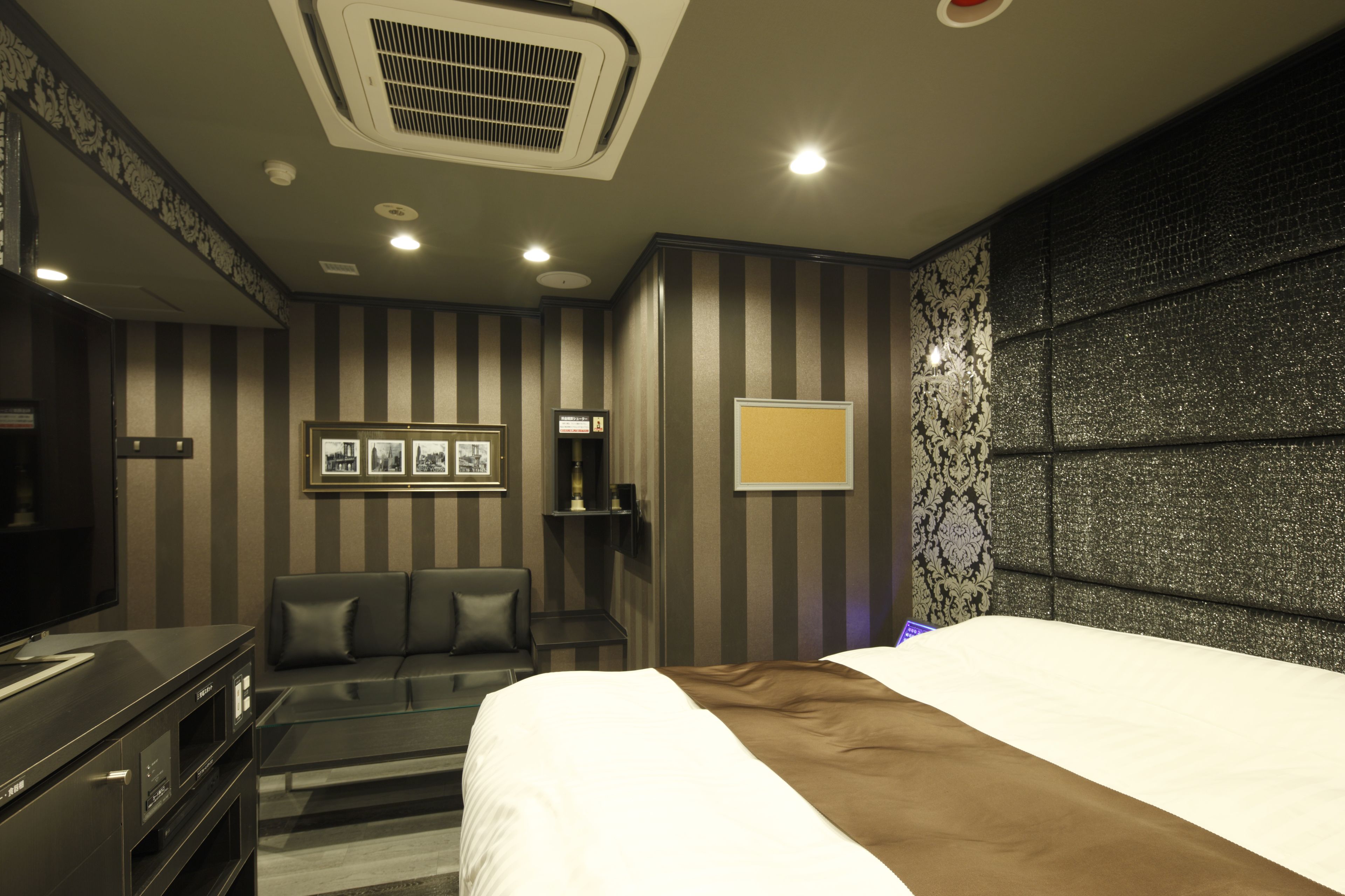 A hotel room with a bed, a TV, a seating area with a sofa and armchairs, a small table, and a decorative wall panel.
