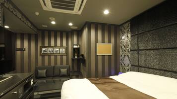 A hotel room with a bed, a TV, a seating area with a sofa and armchairs, a small table, and a decorative wall panel.