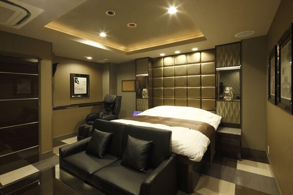 A modern hotel room with a large bed, a black leather sofa, and a seating area with a glass coffee table.