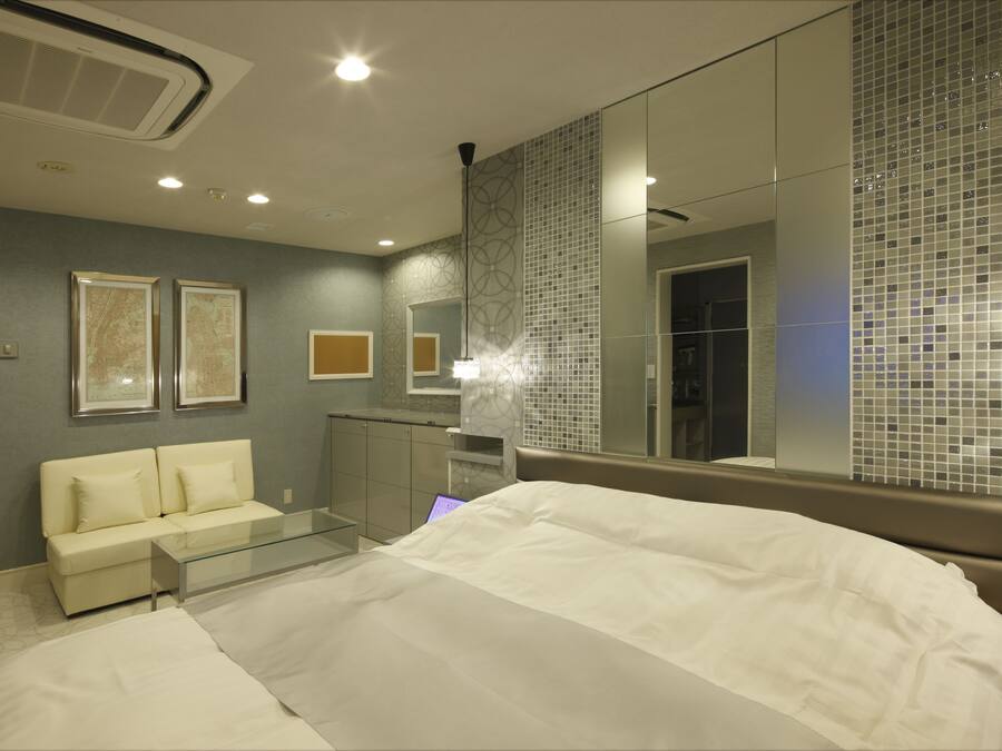 Una habitación de hotel moderna con una cama, una mesa de centro de vidrio, un sofá y un espejo grande.