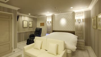 A hotel room with a large bed, a white sofa, a desk with a chair, and a massage chair.