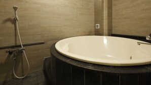 Un baño con una bañera grande y redonda, un cabezal de ducha manual y un espejo fijado a la pared.
