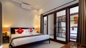 Quarto de hotel com cama, luminárias de cabeceira, uma mesinha de vidro e vista através de uma porta de vidro.