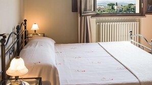 A bedroom with a wooden ceiling, a bed with a floral bedspread, a bedside lamp, a window with curtains, and a view of the landscape. - Super panoramic, private pool, fast Wifi, Air cond, close to town - NO BILLS (Pisa)