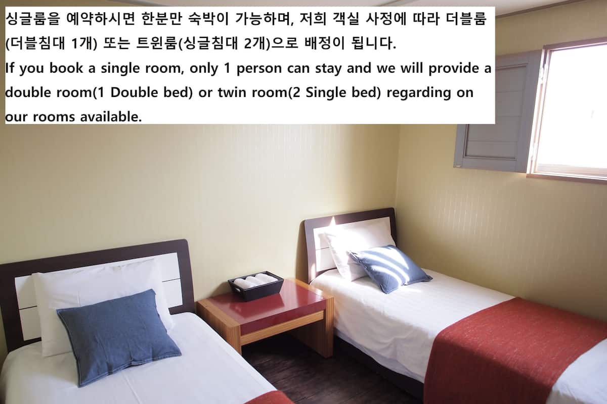 A single room with two beds, each with a pillow and a small bedside table.