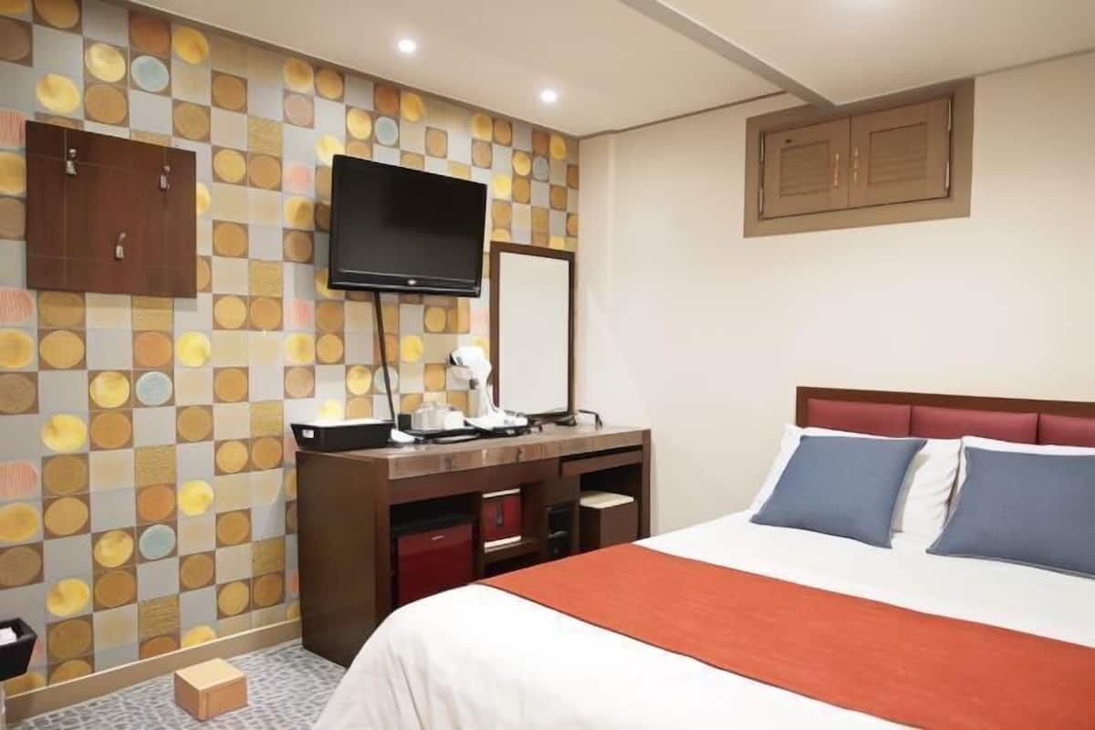 A hotel room with a bed, a desk with a flat-screen TV, a mirror, and a patterned wall.