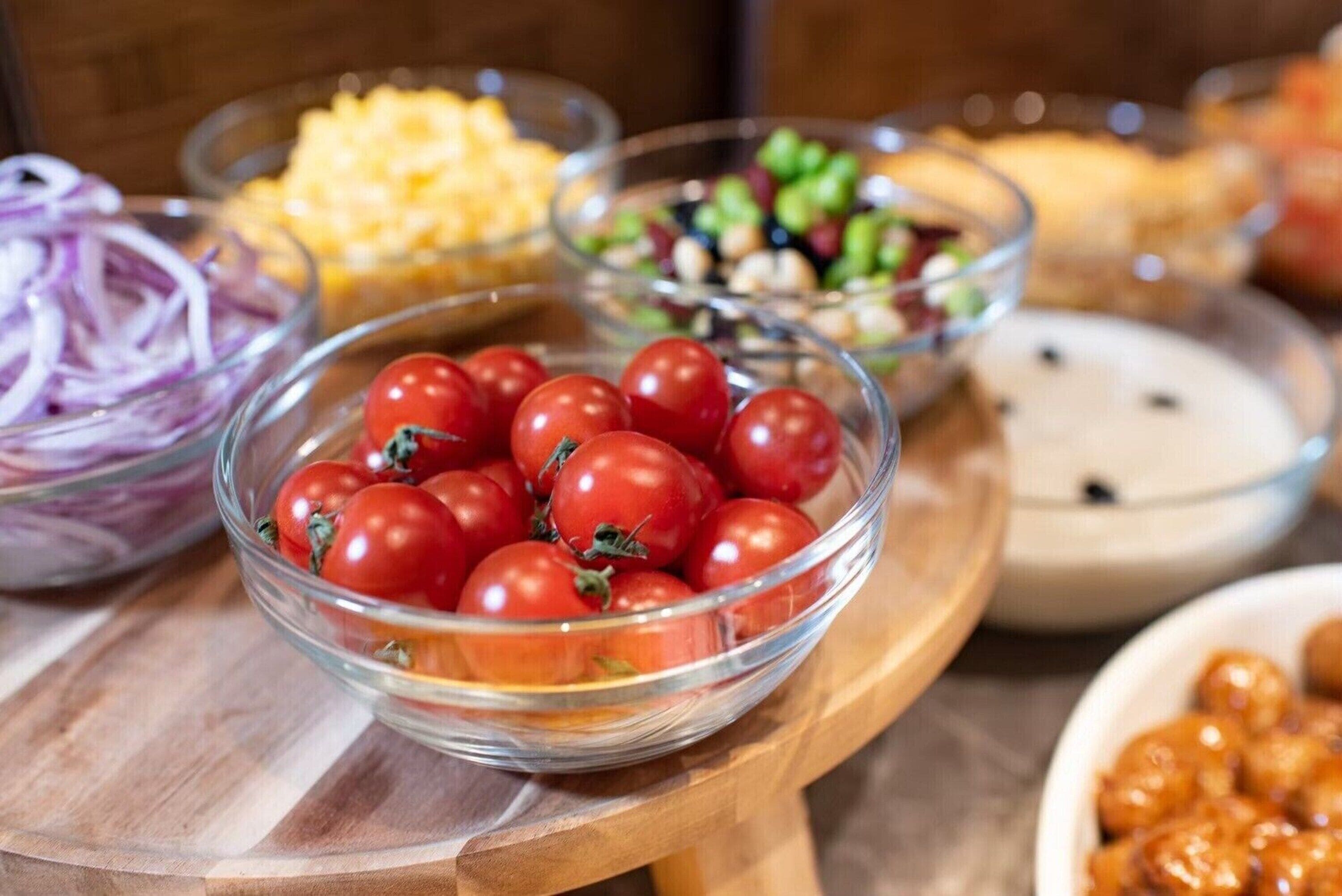 A variety of food items including a bowl of cherry tomatoes, a bowl of sliced red onions, and other dishes in the background.