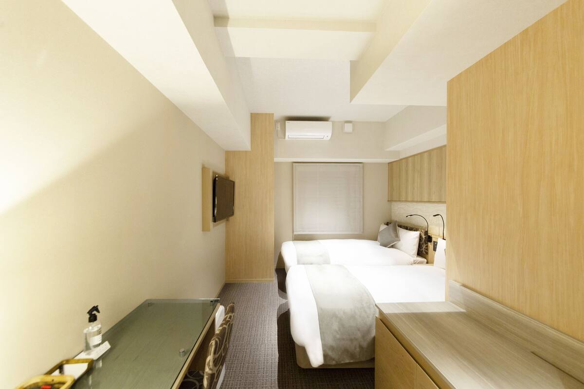 A hotel room with a bed, a desk, a chair, a TV, and a window.
