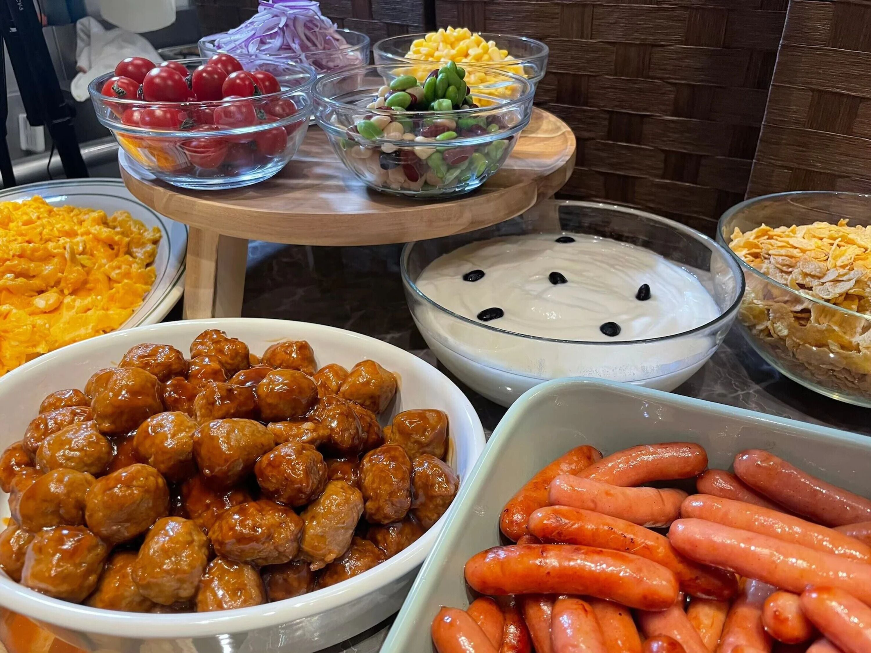 Een buffet met diverse gerechten, waaronder gehaktballetjes, worstjes, mais en een salade.