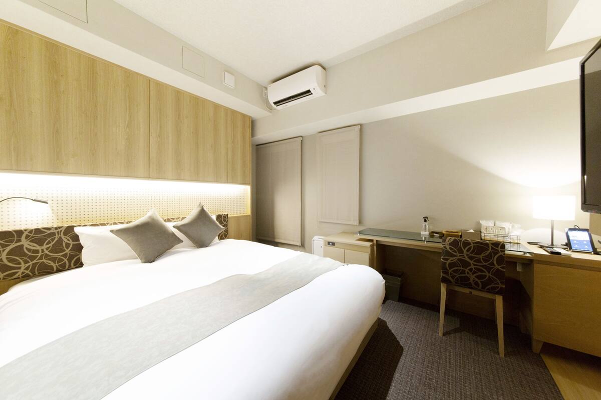 A hotel room with a large bed, a desk, a chair, and a TV.