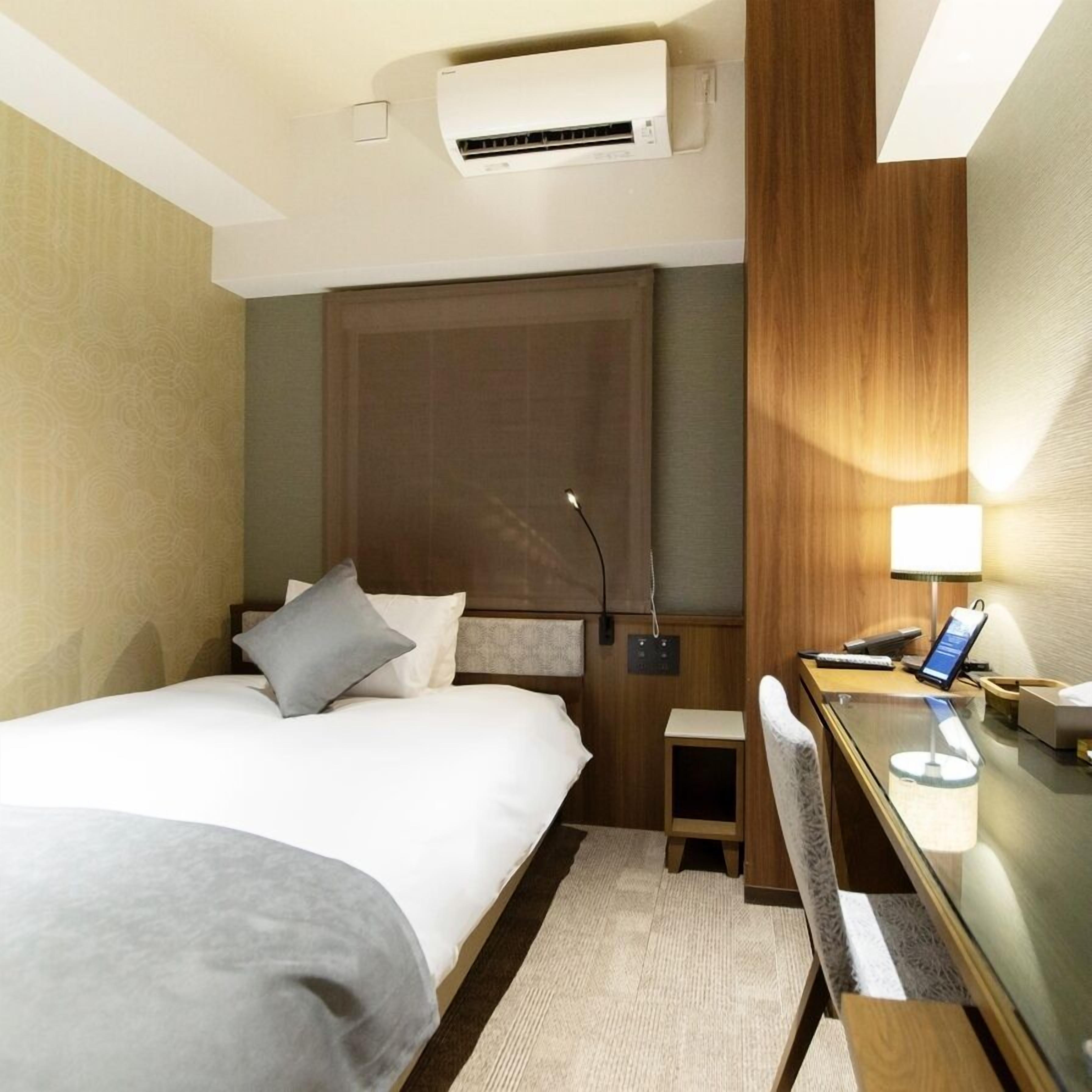 Una camera d'albergo con un letto, un comodino, una lampada e un climatizzatore.