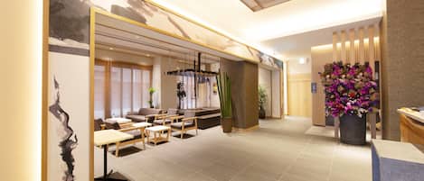 Un interior moderno con mostrador de recepción, zona de estar y una planta grande en maceta.