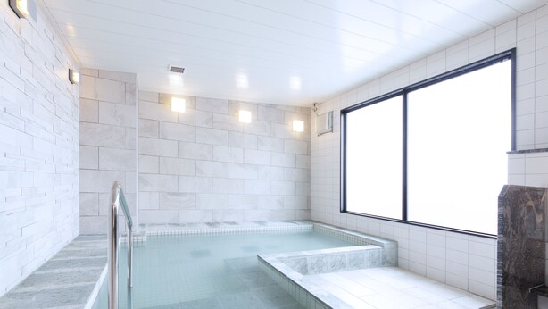 Un área de spa con un ventanal grande, una bañera de hidromasaje con cerramiento de vidrio y suelo de mármol.