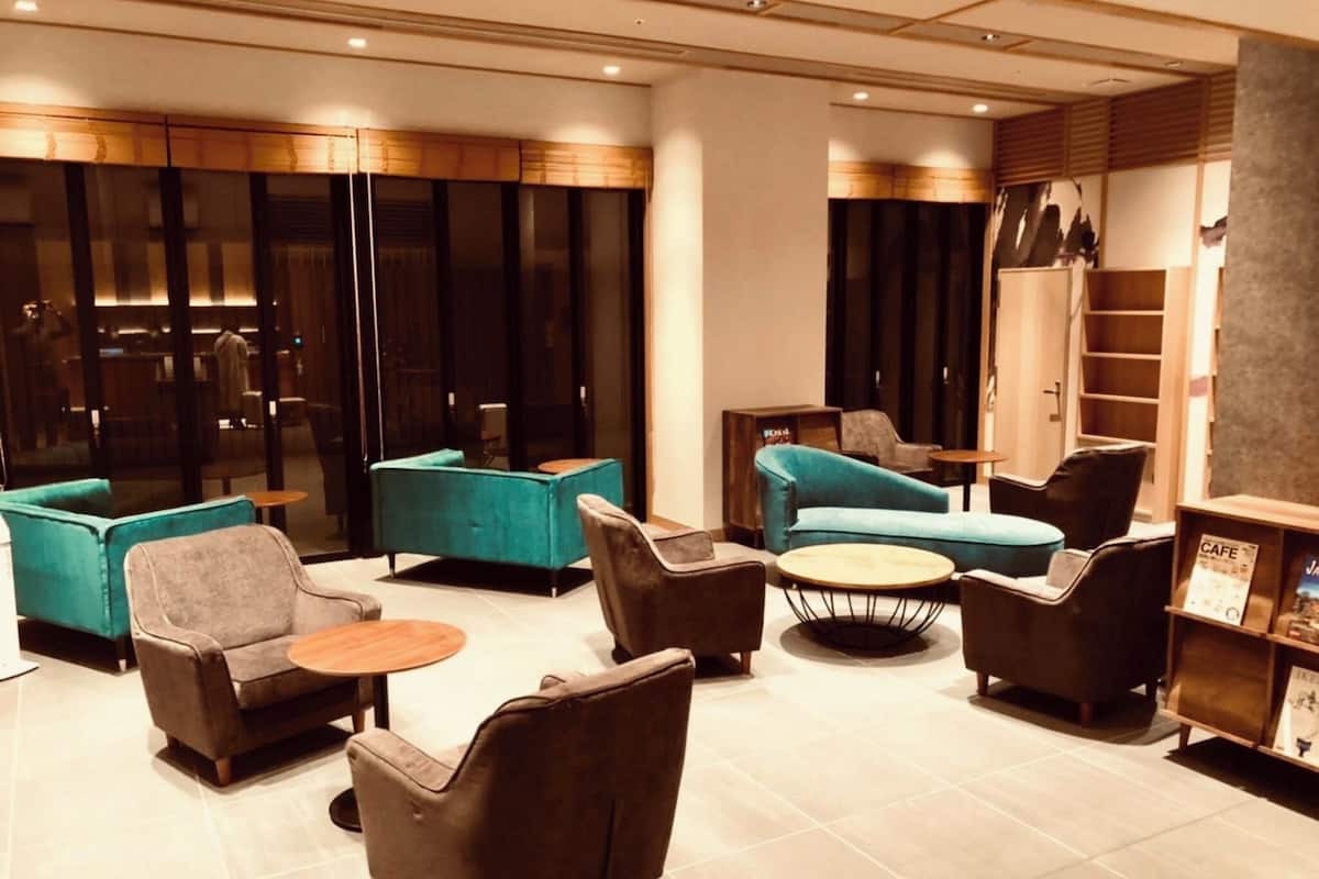 Un área de descanso moderna con sofás, sillones y una mesa de centro, que cuenta con un muro de vidrio y paneles de madera.