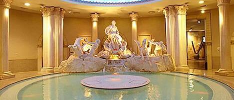 A grand lobby with a central fountain, ornate columns, and a circular reflective pool.