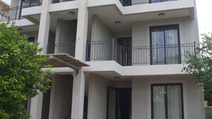 A multi-story building with balconies, a covered entrance, and a brick-paved courtyard with outdoor furniture.