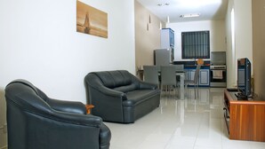 A modern living room with two black leather sofas, a dining area with a table and chairs, and a kitchen with a stove and refrigerator.