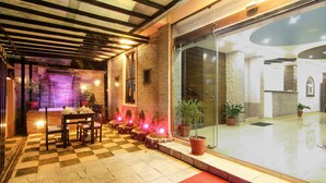 A checkered floor, a table with chairs, potted plants, and a glass door leading to a bright interior. - Hotel Lakeside (Pokhara)