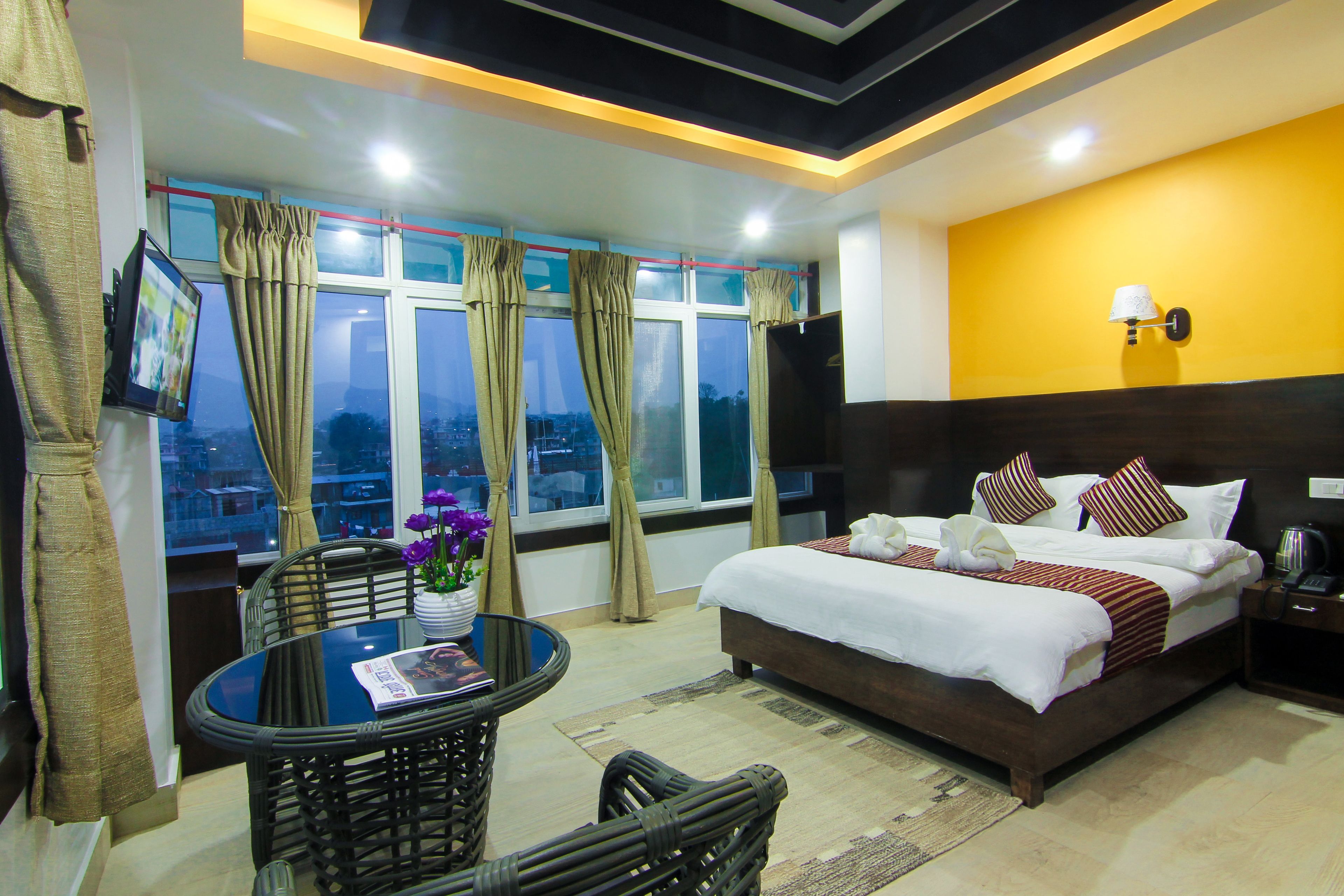 A hotel room with a bed, a table with chairs, a TV, and a window with curtains.